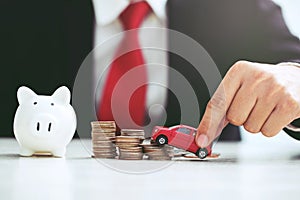 Business man in suit and close up hand holding model of toy car red on over a lot money