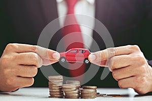 Business man in suit and close up hand holding model of toy car red on over a lot money