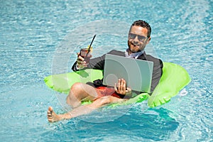 Business man in suit drink summer cocktail and using laptop in swimming pool. Travel business tourism. Office employee