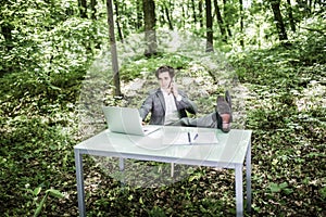 Business man in suit in green park with his legs on office desk talk at mobile phone. Business concept.