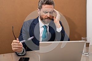 Business man in suit with headache. Tired businessman is working overtime and has headache. Man with laptop at workplace