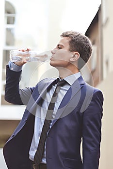 Business man with suit holding water bottle and drinking outdoor. The young Business man drink fresh water in the city