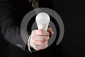 Business man in suit Holding a white light bulb in hand, isolated on gradient black background