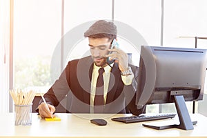 A business man in a suit that is neatly dressed sitting on the phone with a bright smile in the office