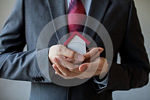 Business man in suit using hands covering and protecting house