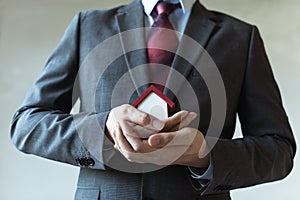 Business man in suit using hands covering and protecting house