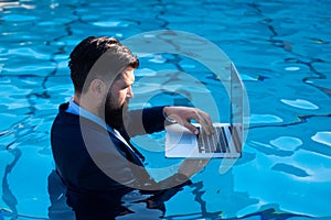 Business man in suit working on laptop from the swimming pool. Funny businessman relaxing with laptop.