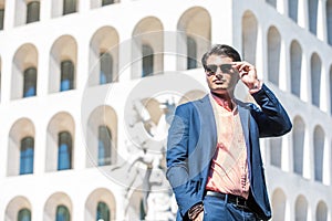 Business man with sunglasses. He blue jacket and shirt. In the background a building