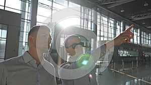 Business man in sunglasses pointing something to his colleague. Two young businessmen looking at flight schedule at