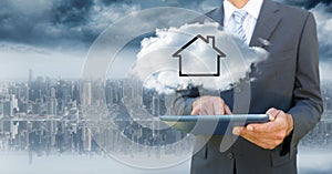 Business man with tablet and cloud with house against blurry skyline