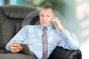 Business man talking on a mobile phone and working on his tablet