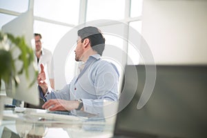 Business man talking to a colleague sitting at his Desk