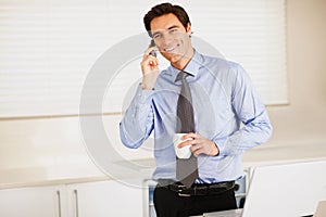 Business man using cellphone with a laptop while at the kitchen. Happy young business man using cellphone with a laptop