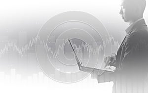 Business man using laptop with abstract financial chart and up trend line graph in stock market on black and whit color background