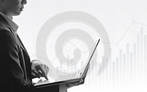Business man using laptop with abstract financial chart and uptrend line graph in stock market on black and white color background