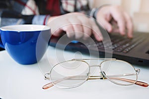 Business man using laptop computer and hand typing on laptop keyboard with notebook pen glasses and cup of hot coffee