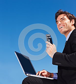 business man using a laptop while holding a mobile phone. Successful young business man using a laptop while holding a
