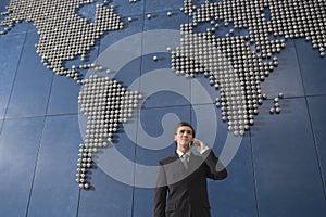 Business man using mobile phone in front of world map in office
