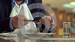 Business man using mobile phone and making photo food in restaurant