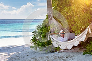 A business man on vacation works on his laptop on a tropical beach