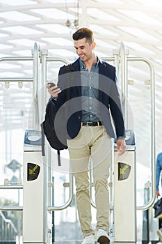 Business man walking through turnstile with mobile phone