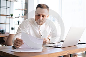 Business man wearing casual clothing is typing on laptop computer and working with paper document