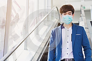 The business man wearing protection face mask against coronavirus, PM 2.5 and cold while standing on escalator. Coronavirus and