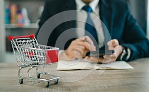 Business man wearing suit and calculates the budget. Shopping cart a on table with mobile. Budget of poor low income family.