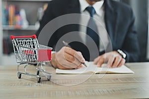 Business man wearing suit and calculates the budget. Shopping cart a on table with note book. Budget of poor low income family.