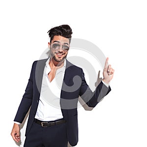 Business man wearing sunglasses smiling and pointing up