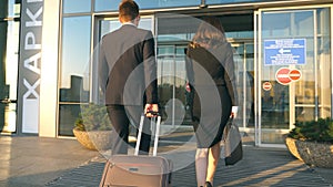 Business man and woman going to the airport with their luggage. Young businessman carrying suitcase on wheels and