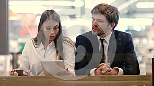 Business man and woman sitting using tablet in a mall.