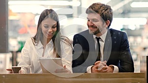 Business man and woman sitting using tablet in a mall.