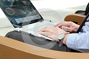 Business man working and analyzing financial figures on a graphs on a laptop outside.