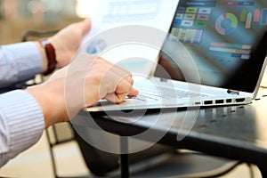 Business man working and analyzing financial figures on a graphs on a laptop outside.