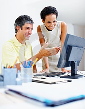 Business man working on computer with colleague. Smiling business man pointing at computer screen and showing something