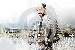 Business man working with digital tablet over city and nature landscape background. Corruption and speculation concept