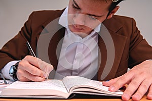 Business man writing his notes in a notebook. Elegant man dressed in a brown suit, a white shirt and glasses. Lawyer working in