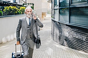 Business manager talking on smart phone while walking with suitcase and bag taking on a business travel