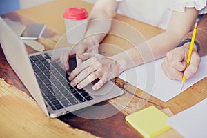 Business meeting in modern office, close-up of woman hands on keyboard laptop on wooden table, man hand writing by pencil.