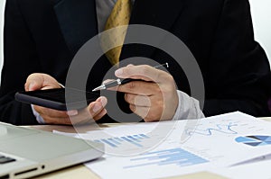 Business men hand holding cell phones and pens on the desk