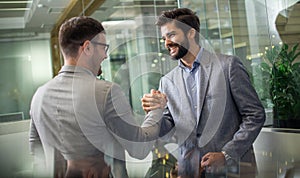 Business men with hands in a joint handshake gathered into a fist celebrating success at modern glass office.