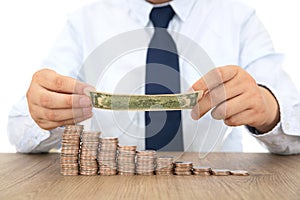 Business men`s hand holding a dollar bill to cover and protect a row of declining dollar coins on the table