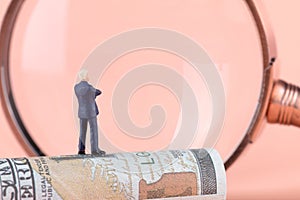 Business men standing on dollar bills looking through a magnifying glass