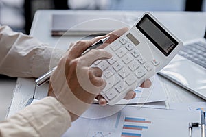 Business men using a calculator to calculate numbers on a company`s financial documents, he is analyzing historical financial dat