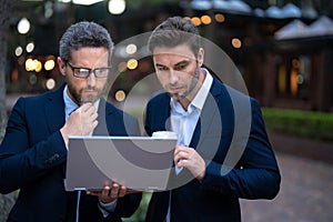 Business mens with takeaway coffee and laptop outdoor. Business men team using laptop outdoor. Businessmen looking