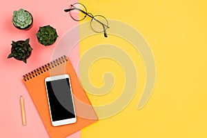 Business mockup with smartphone with black copyspace screen, succulent flowers, glasses and notebook, pastel pink and yellow backg