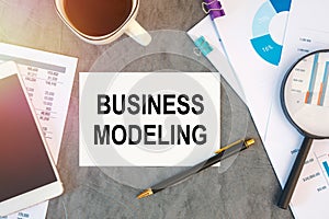 BUSINESS MODELING is written in a document on the office desk, coffee, diagram and smartfon