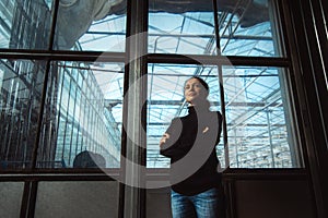 Business in modern greenhouses. A young woman entrepreneur stands with her arms folded on her chest, in front of the gate to a new