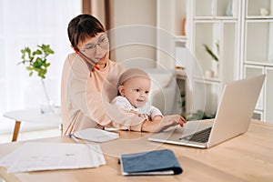Business mom working remotely on laptop while taking care of her baby